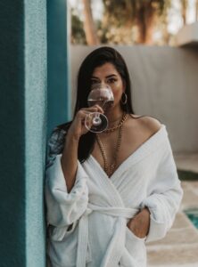 Chic woman in bathrobe enjoying wine outdoors, exuding elegance and relaxation.