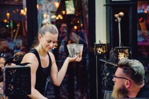 Waitress serves drinks at an outdoor cafe during a lively evening, creating a warm social ambiance.
