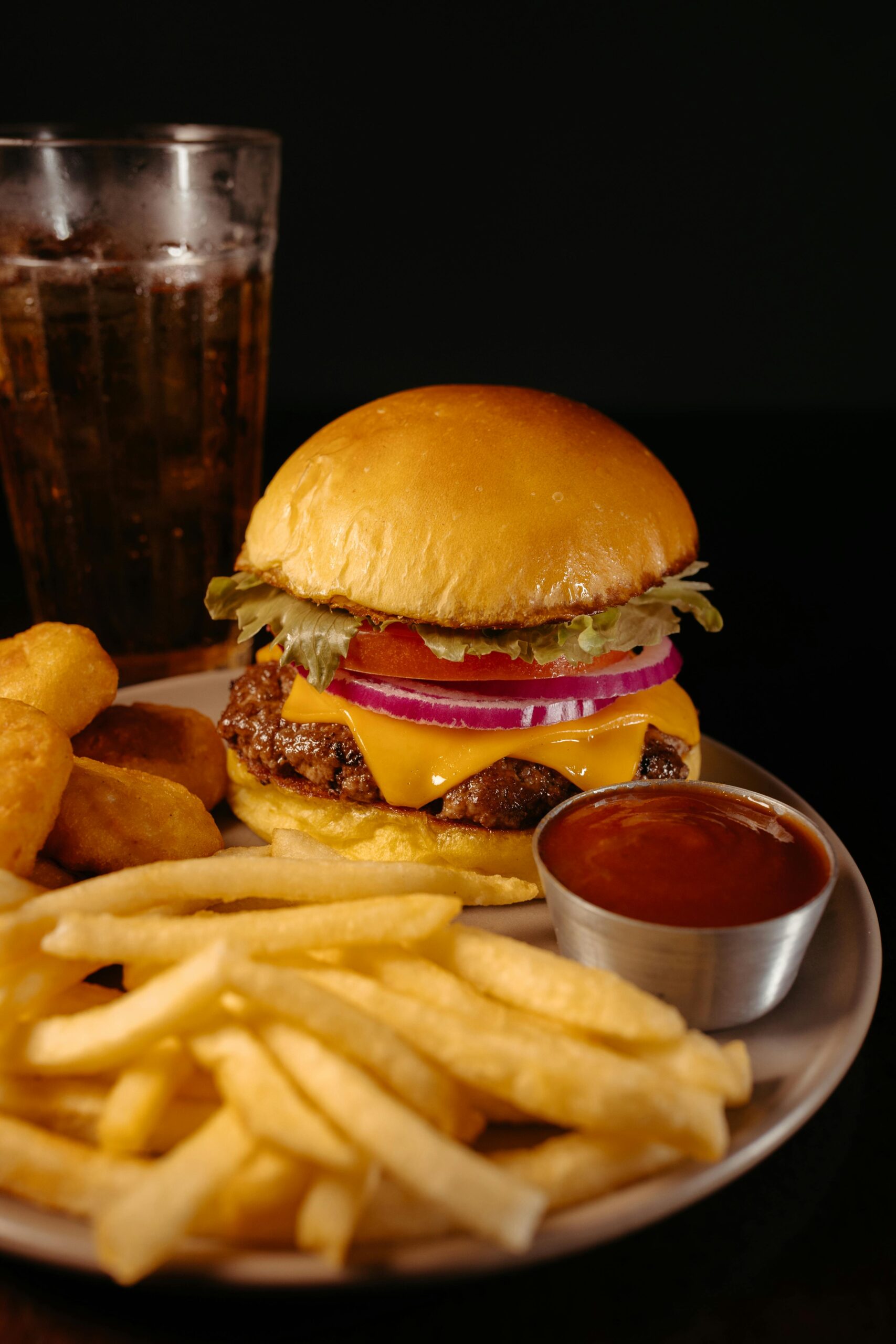 Delicious cheeseburger with sides of french fries and nuggets, served with soda.
