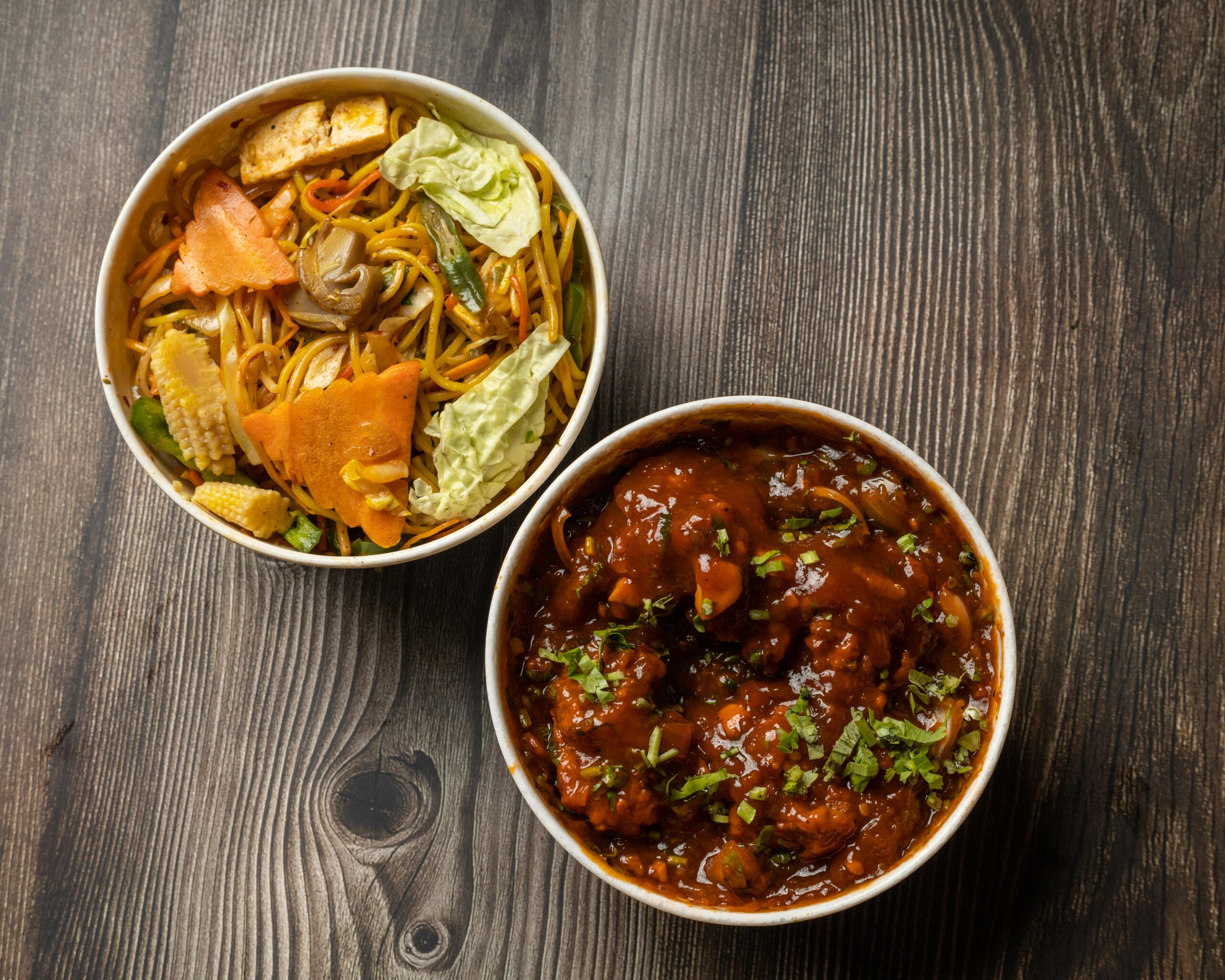 Top view of flavorful Indo-Chinese noodles and Manchurian curry on a rustic wooden table.