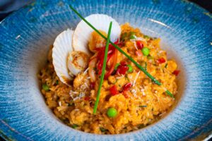Rich and creamy seafood risotto topped with seared scallops, vibrant vegetables, and fresh herbs.