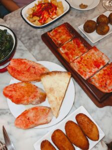 A vibrant spread of Spanish tapas including patatas bravas, bread with tomato, and croquettes on a marble table.