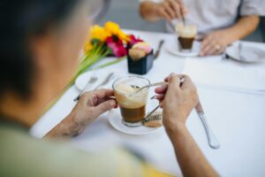 Senior couple stirring coffee at an outdoor cafe. Bright flower decor adds a cheerful touch.