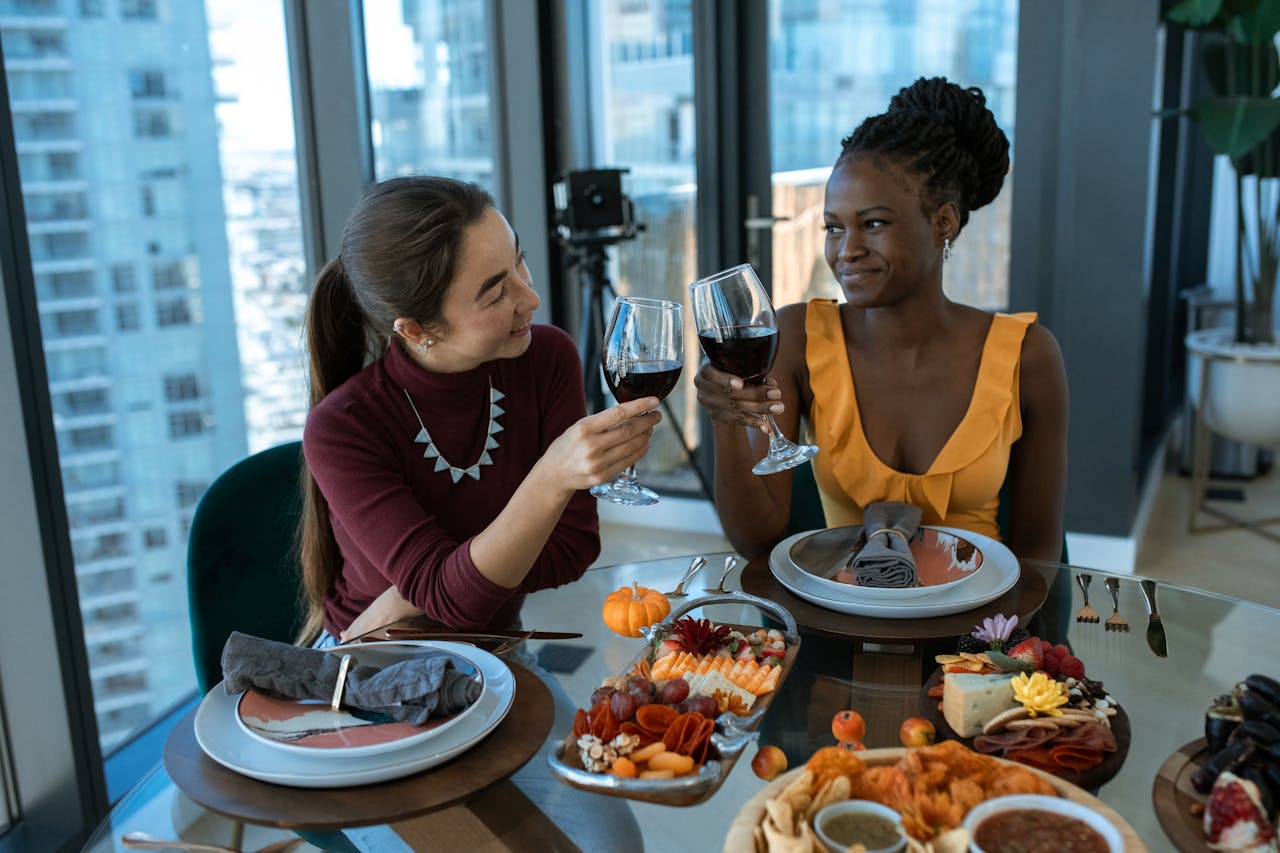 Two friends toast with wine over a beautifully arranged charcuterie and cheese platter.