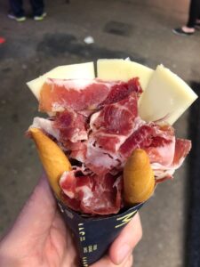 Hand holding a cone of jamón and cheese, typical Barcelona street food.