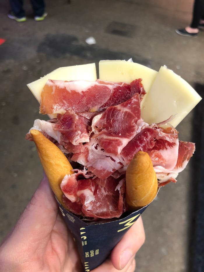 Hand holding a cone of jamón and cheese, typical Barcelona street food.