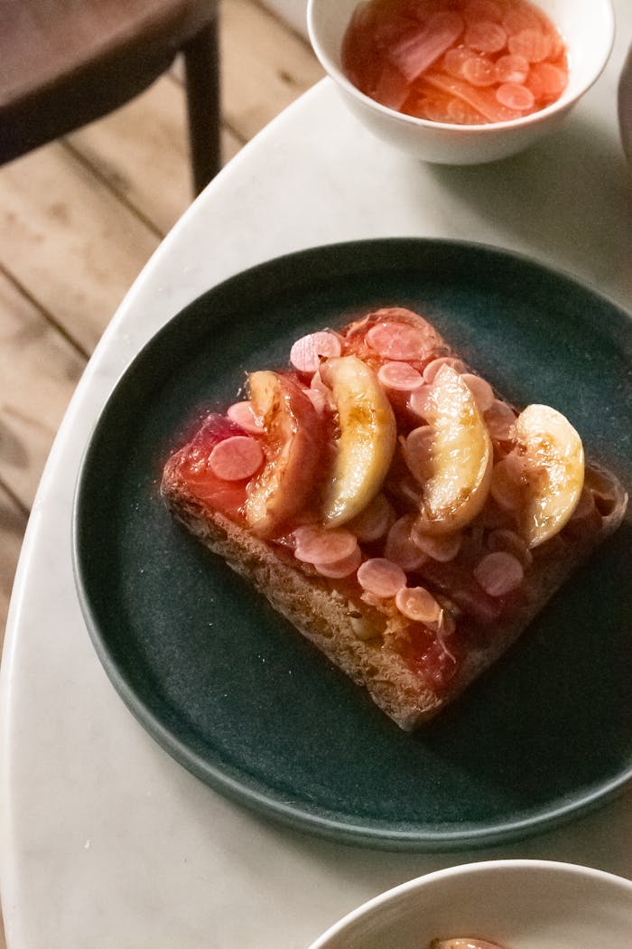 Delectable slice of toast topped with fresh fruit on a dark plate, perfect as a dessert or snack.