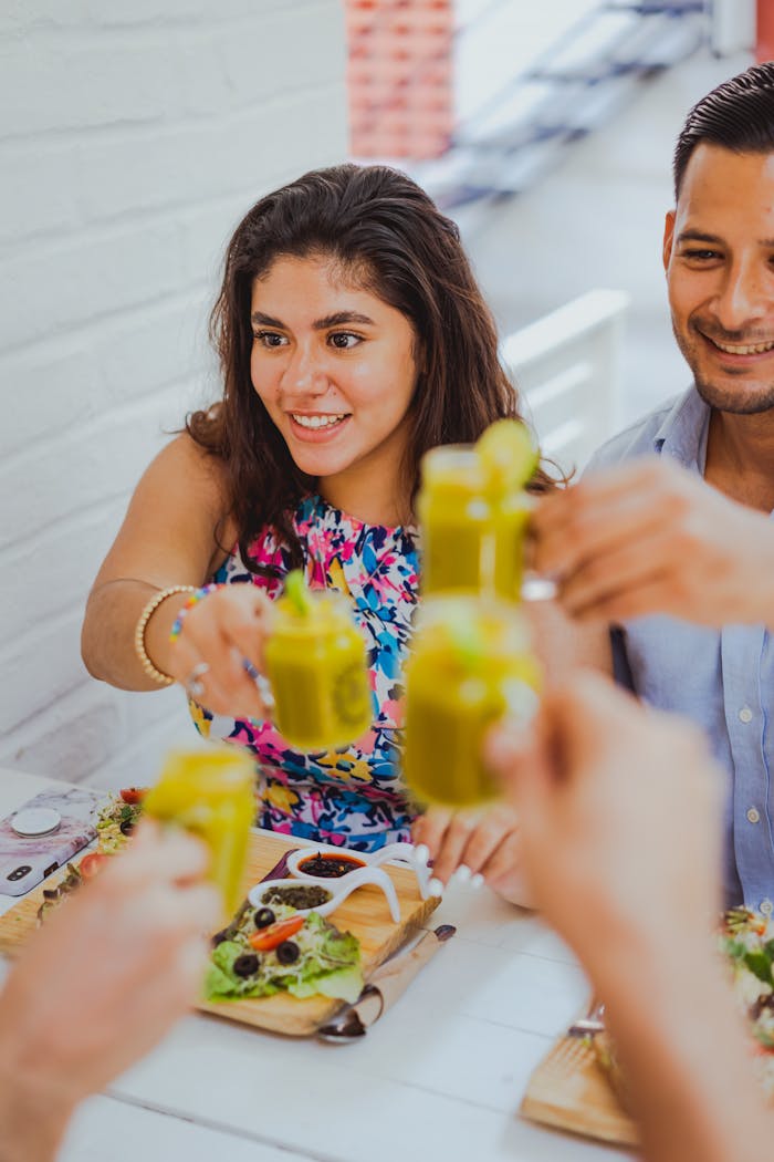 Friends enjoying a toast with green smoothies over a fresh salad meal outdoors.