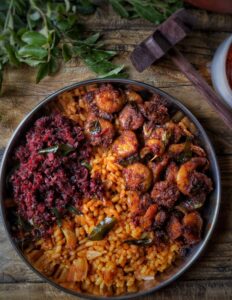 Close-up of spiced rice and prawns garnished with curry leaves on a rustic wooden table.